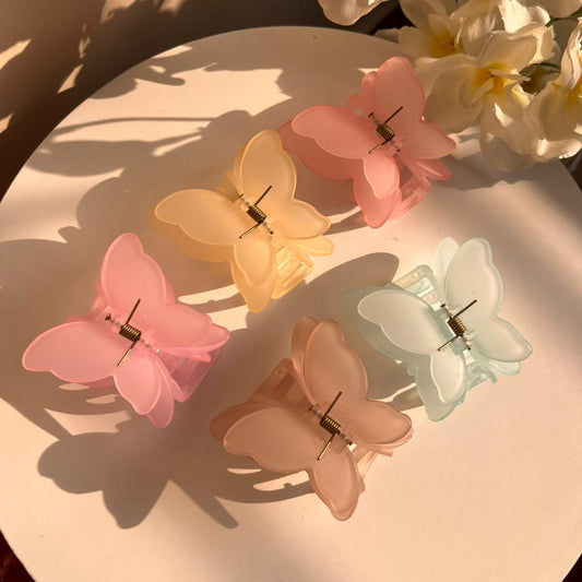 Butterfly-shaped hair clips in pastel colors on a white surface with flowers in the background.