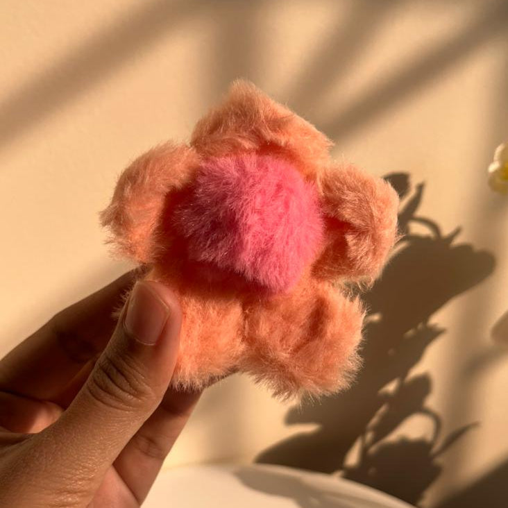 Hand holding a fluffy peach flower-shaped hair clip against a neutral background
