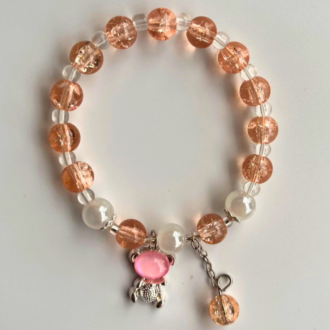 Bracelet with peach and white beads and a pink cat charm on a light gray background