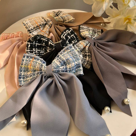 Decorative bows with ribbons and pearls on a white plate with flowers in the background