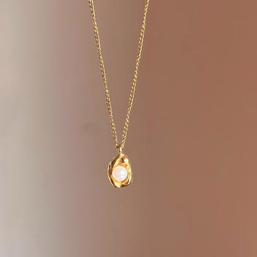 Gold necklace with a teardrop-shaped pendant on a plain background