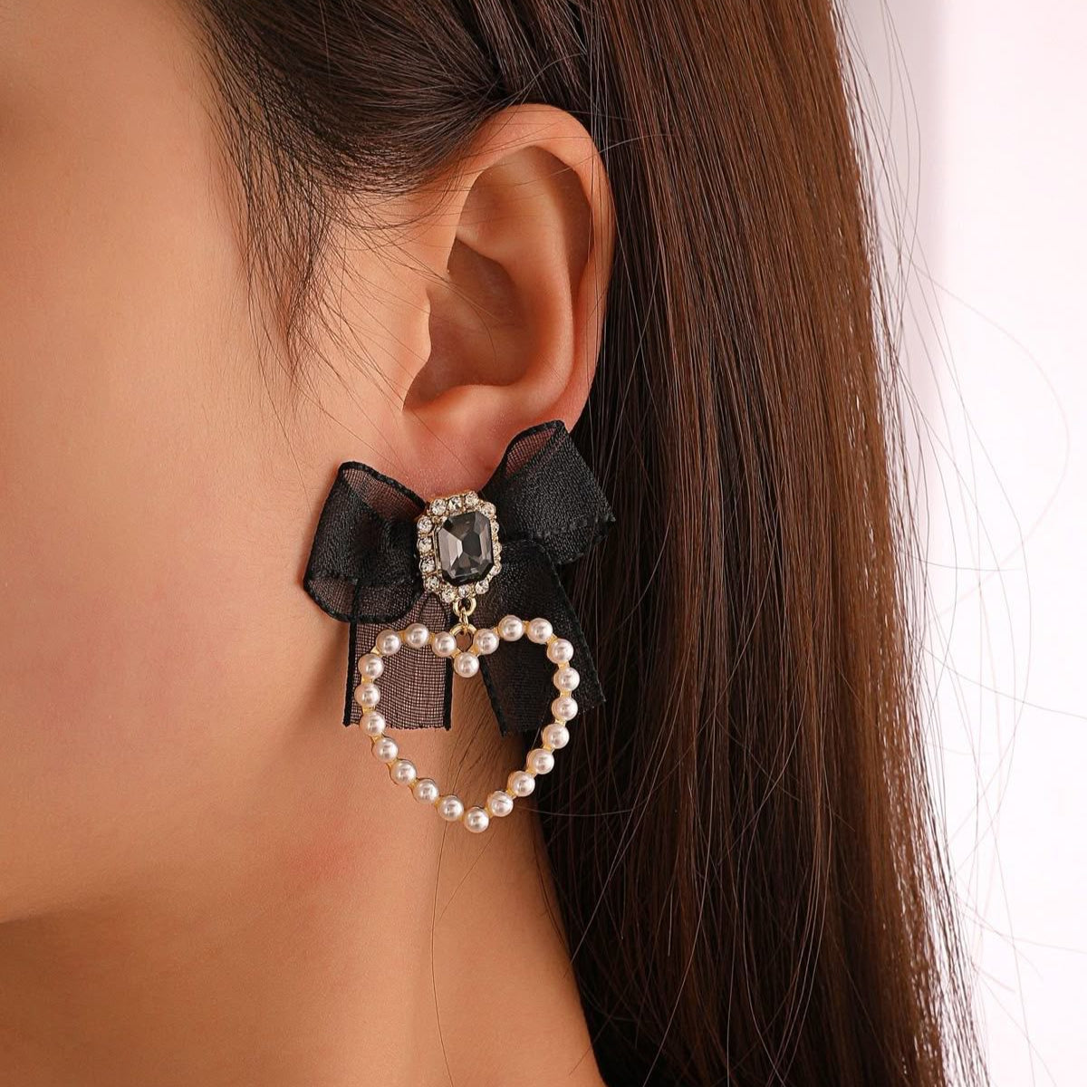 Earring with black bow and heart design worn by a person