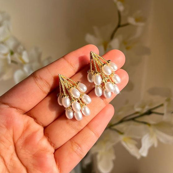 Hand holding a pair of pearl earrings with a soft background