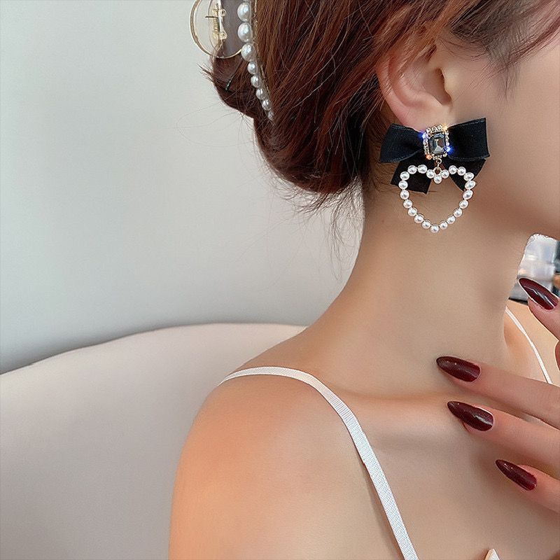 Heart-shaped earring with pearls worn by a person against a neutral background
