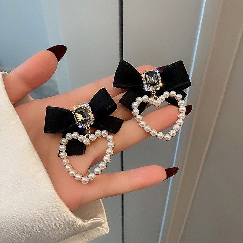 Hand holding two decorative heart shaped earrings with a satin bow and pearl detailing.