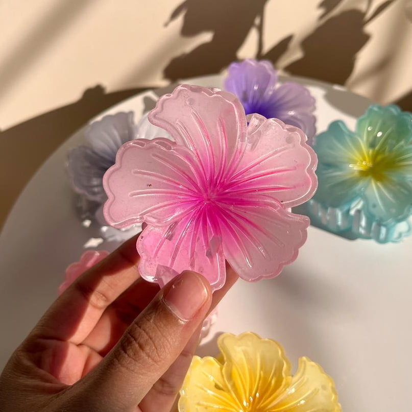 Hand holding a pink flower-shaped hair clip with other colorful flowers in the background.