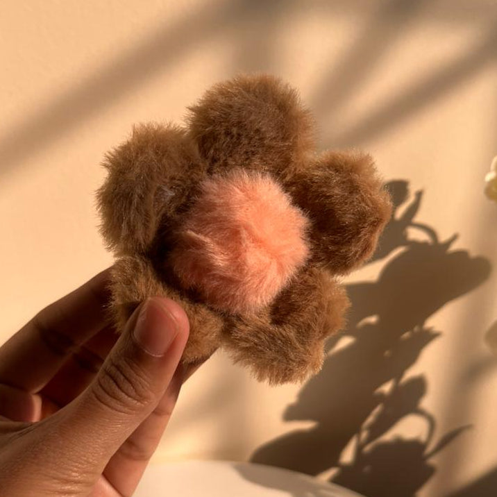 Brown flower-shaped hair clip held by a hand against a beige background