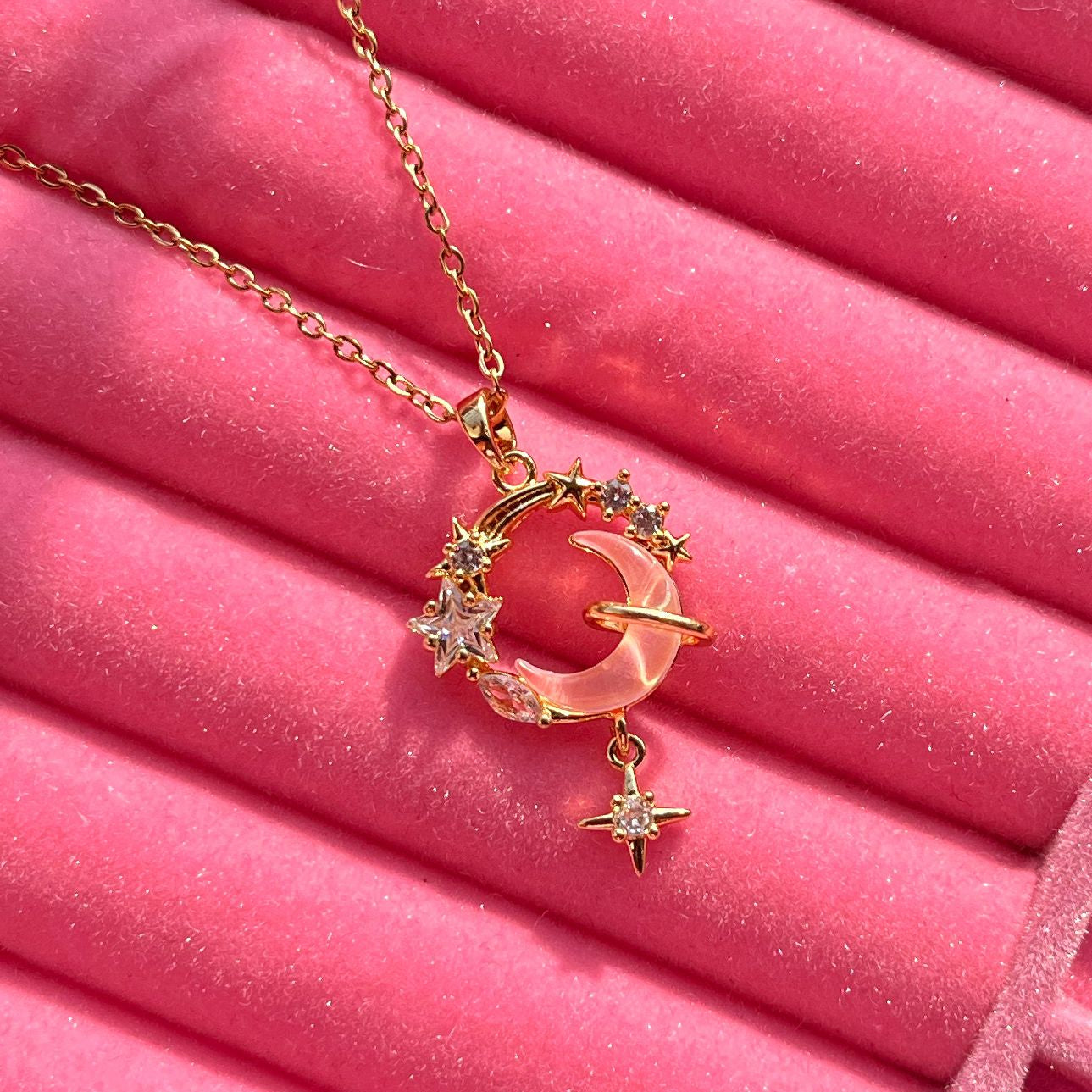 Gold necklace with a crescent moon and star pendant on a pink background