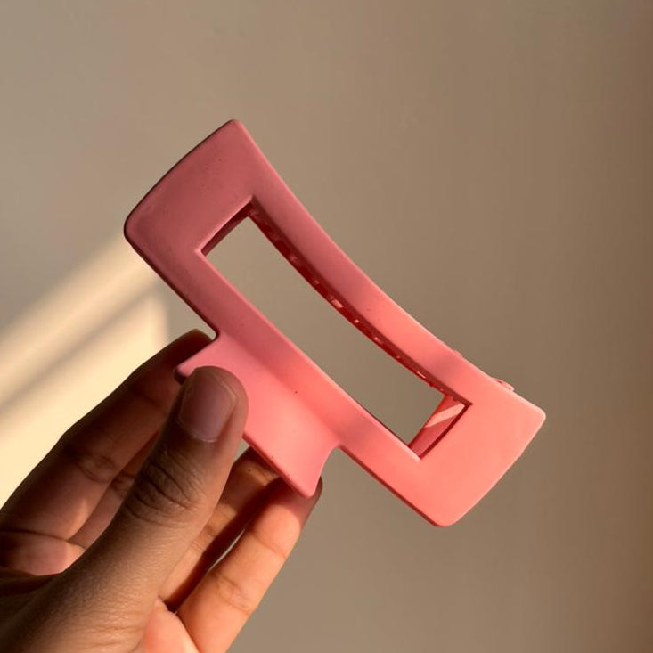 Hand holding a pink rectangular hair clip against a neutral background