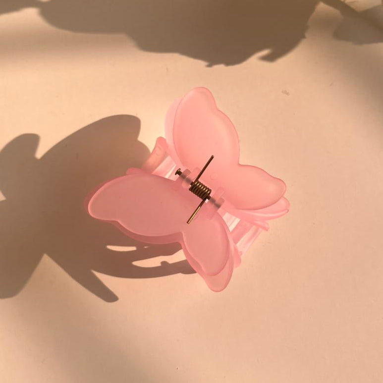 Pink butterfly hair clip on a light pink surface with shadows
