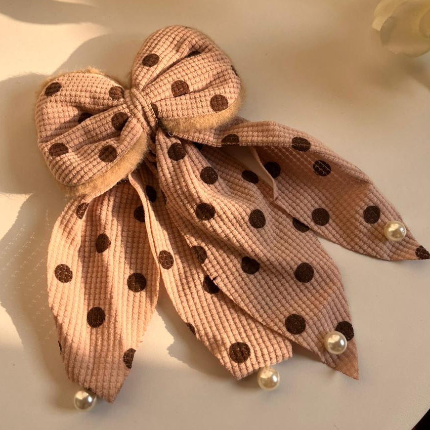 Polka dot bow hair clip on a white surface with a blurred background