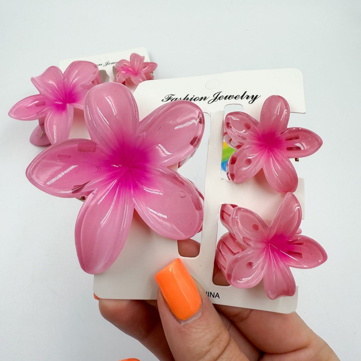 Pink flower-shaped hair clips on a white card held by a hand with orange nail polish.