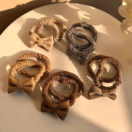 Set of brown hair ties with bows on a white plate, with flowers in the background.