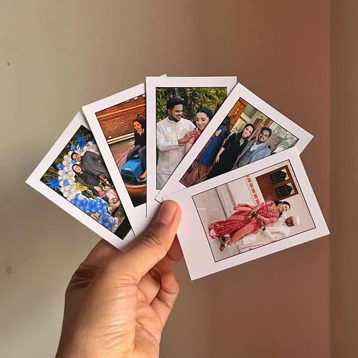 Hand holding four small photo prints against a plain background