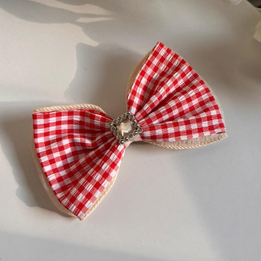 Red and white checkered bow with a decorative center on a light surface.