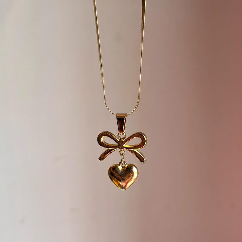 Gold necklace with a heart and bow pendant on a plain background