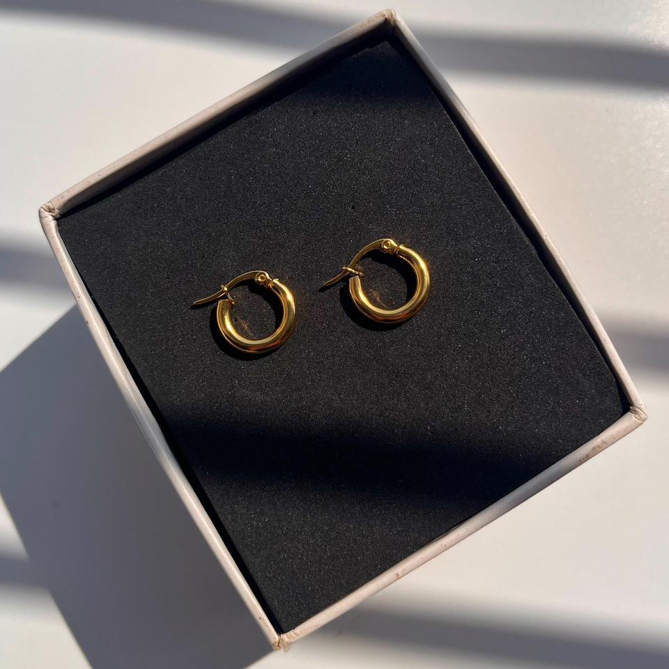 Gold hoop earrings in a black jewelry box on a light surface