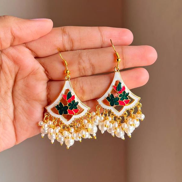 Hand holding a pair of decorative earrings with a plain background