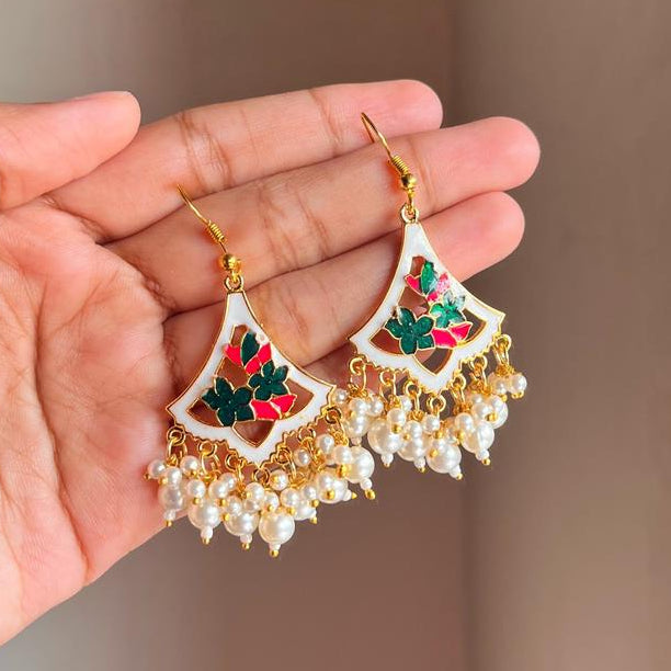 Decorative earrings held by a hand against a neutral background