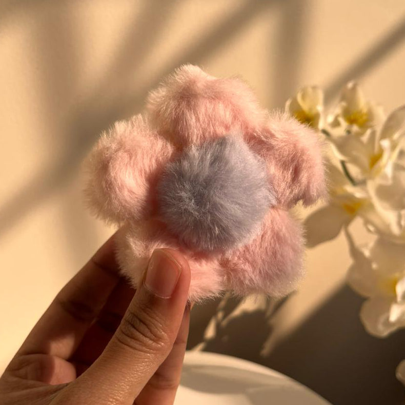 Pink and grey fluffy flower-shaped hair clip held by a hand with a blurred background