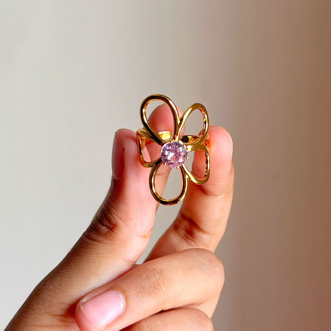 Gold ring with a pink ringheld by a hand against a neutral background