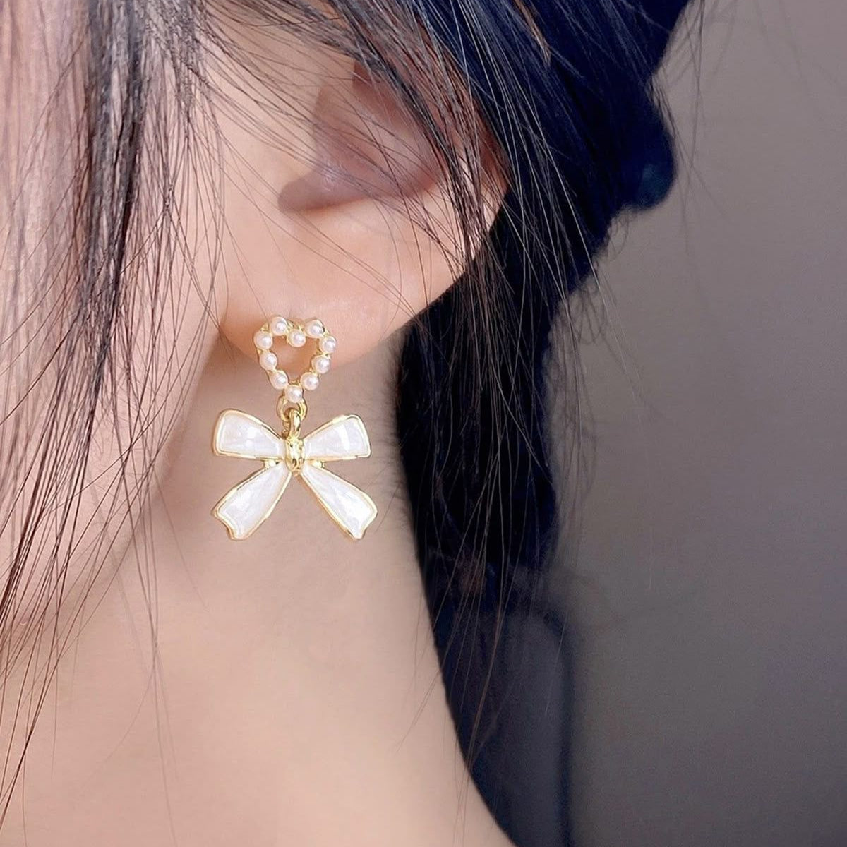 Pearl bow-shaped earrings worn by a person with a neutral background