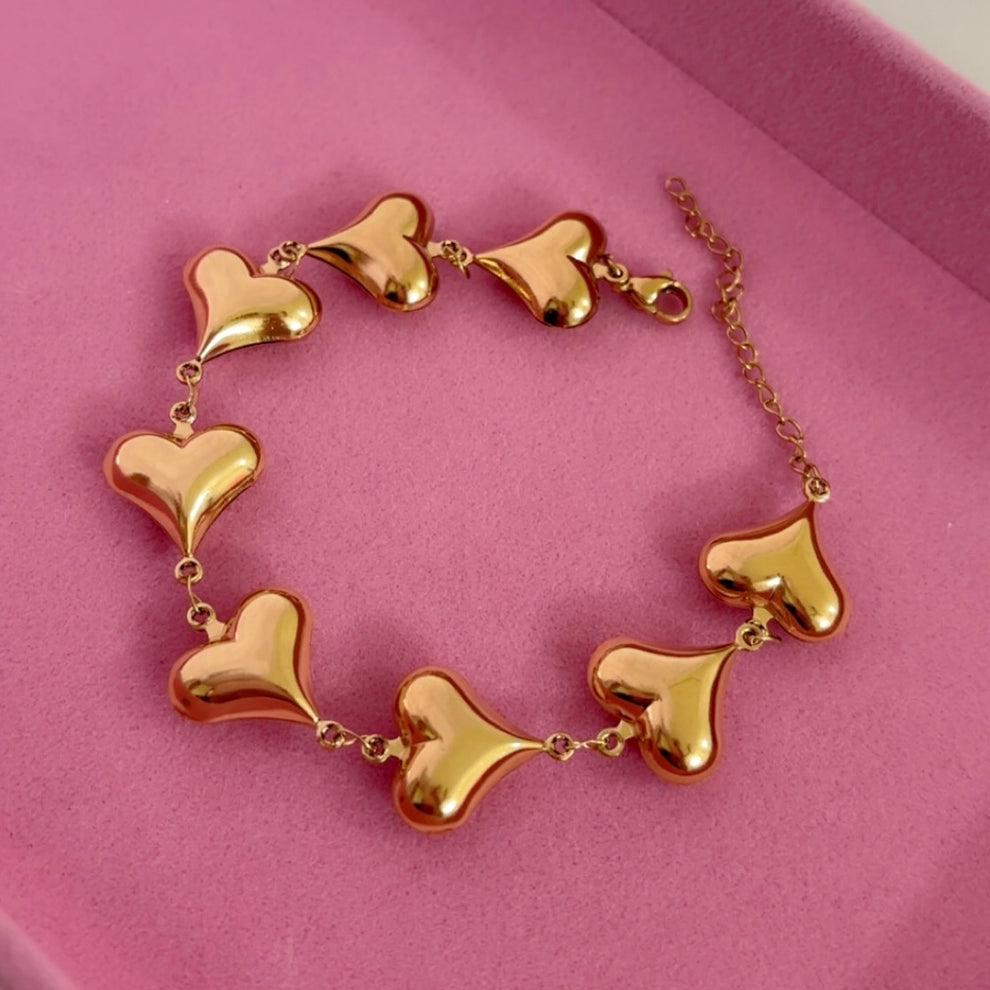 Gold heart-shaped bracelet on a pink background
