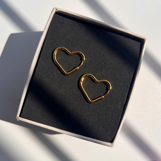 Gold heart-shaped earrings in a black box on a light surface