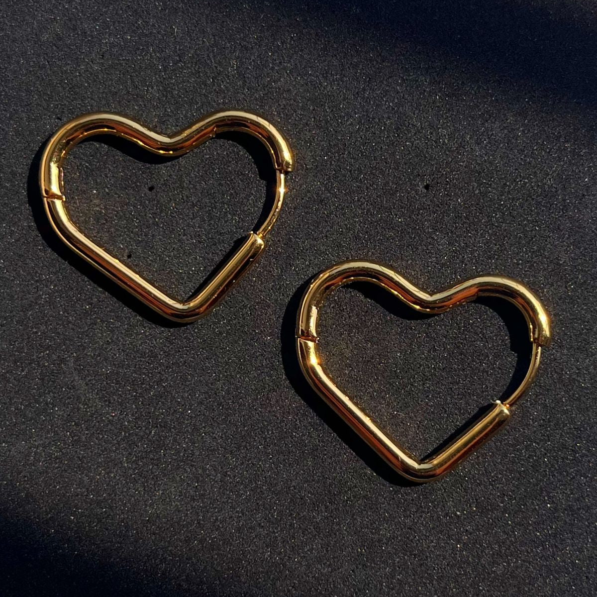Gold heart-shaped hoop earrings on a black background