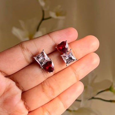 Hand holding two small red and white earrings with a neutral background