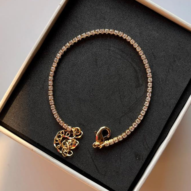 Gold bracelet with a heart charm in a black box on a light surface