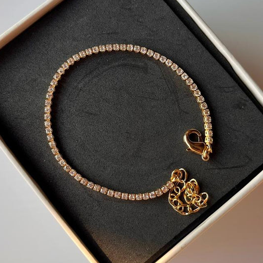 Gold bracelet with a heart charm in a box on a gray background