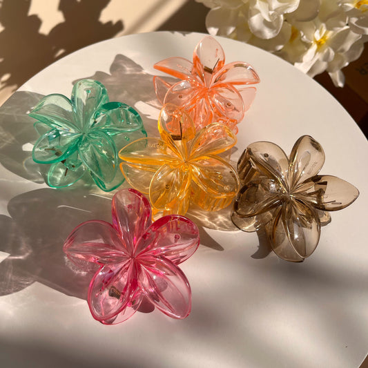 Set of colorful flower-shaped hair clips on a white surface with flowers in the background.