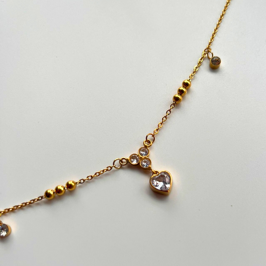Gold bracelet with heart-shaped pendant on a light gray background