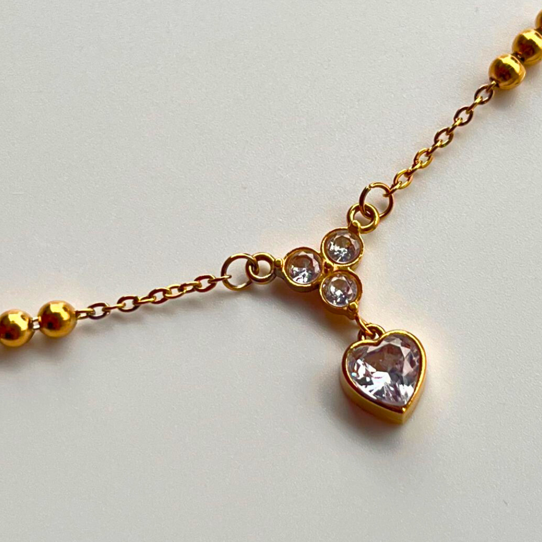 Gold bracelet with a heart-shaped charm on a light gray background