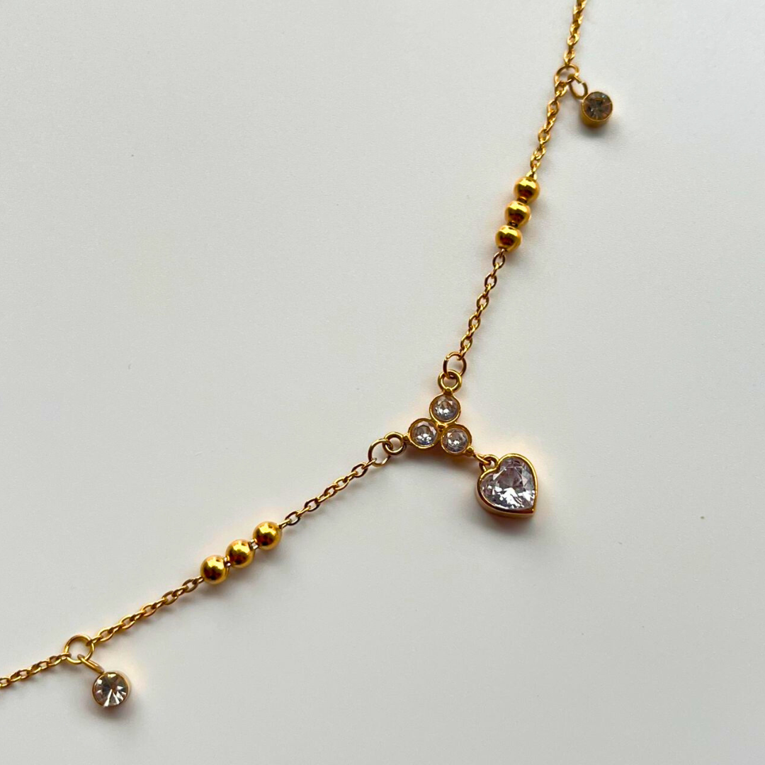 Gold bracelet with heart-shaped pendant on a light gray background