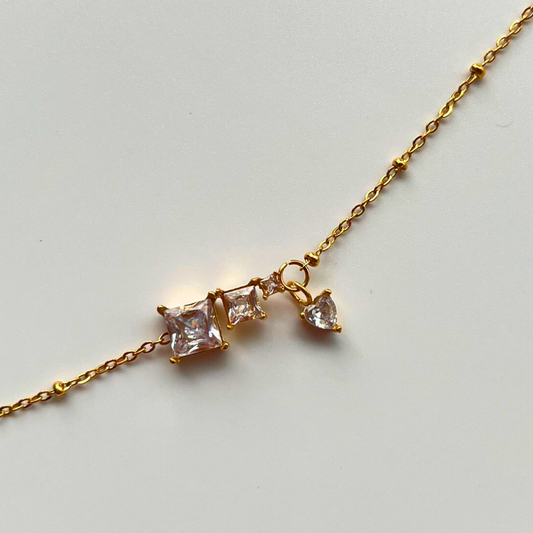 Gold bracelet with three diamond pendants on a light gray background