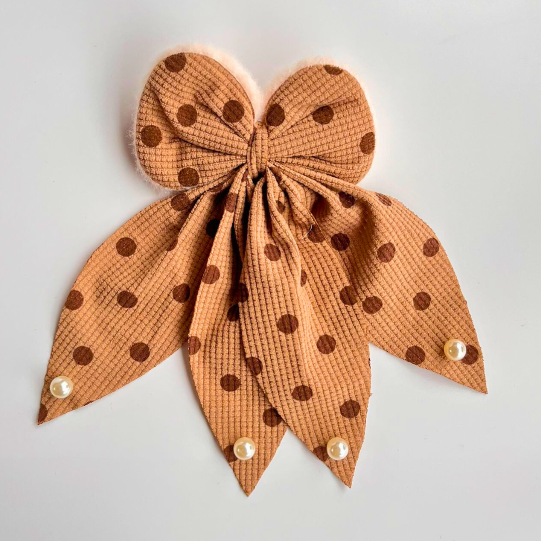 Brown polka dot bow with pearl centers on a light gray background