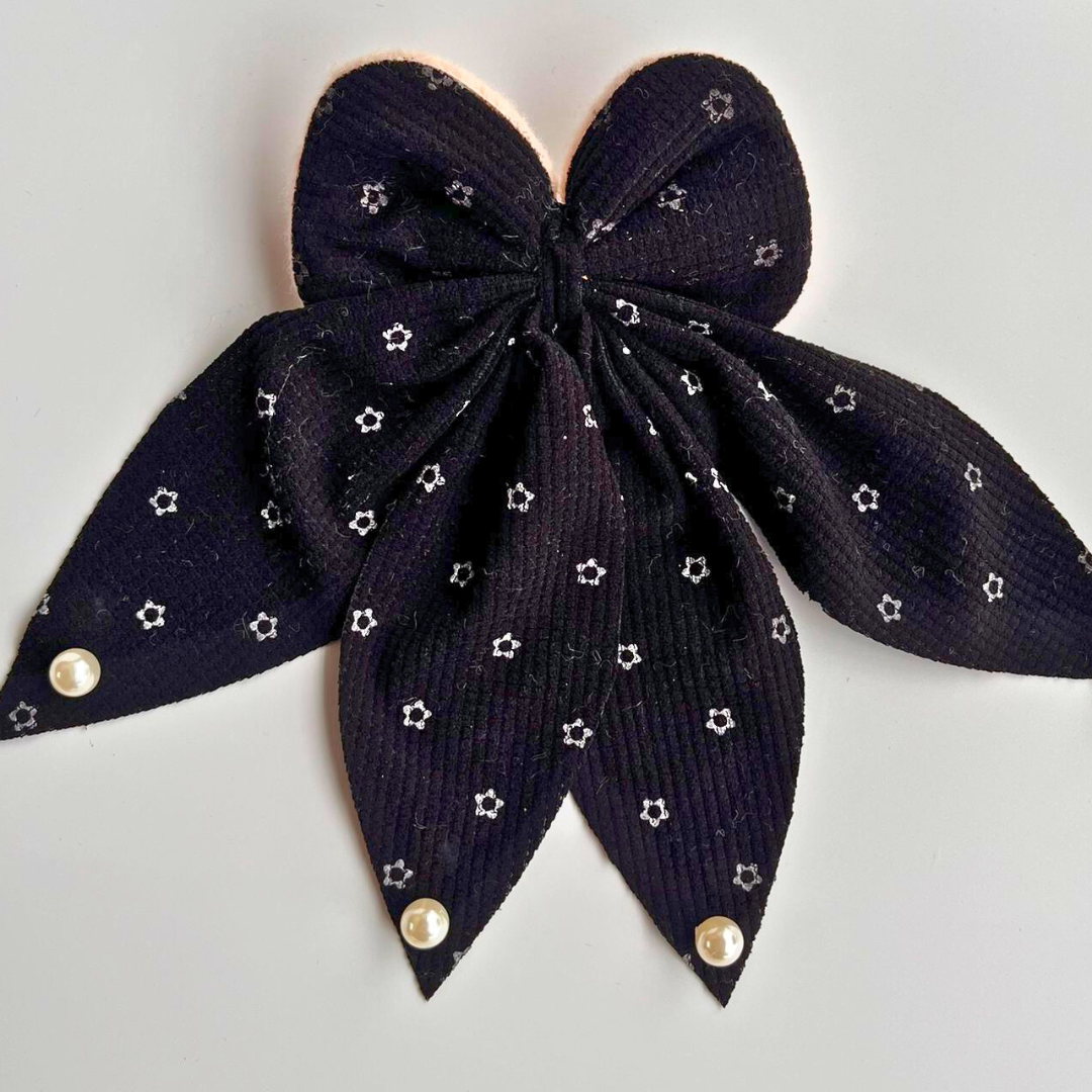 Navy blue bow hair clip with star patterns and gold buttons on a light gray background