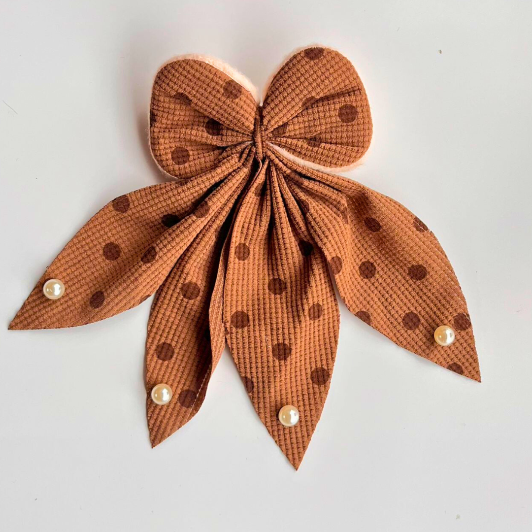 Brown polka dot bow with pearl centers on a light gray background