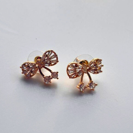 Rose gold bow-shaped earrings with clear gemstones on a light gray background