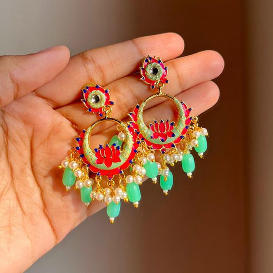 Hand holding decorative earrings with intricate designs and colorful stones against a neutral background
