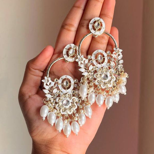 Hand holding a pair of ornate earrings against a neutral background