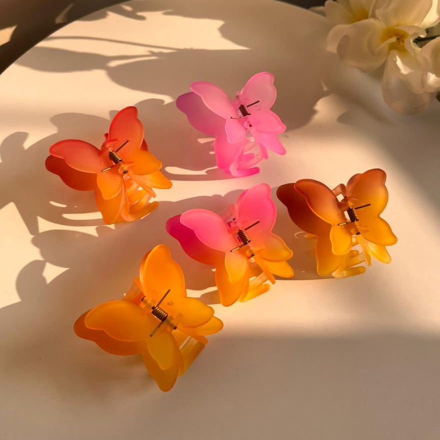 Butterfly-shaped hair clips in orange, pink, and yellow on a white plate with flowers in the background.