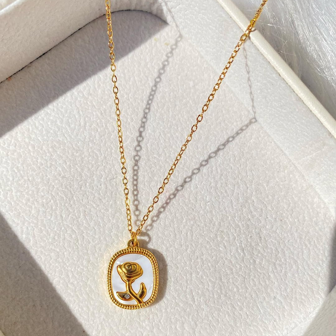 Gold necklace with a rose pendant on a light gray surface