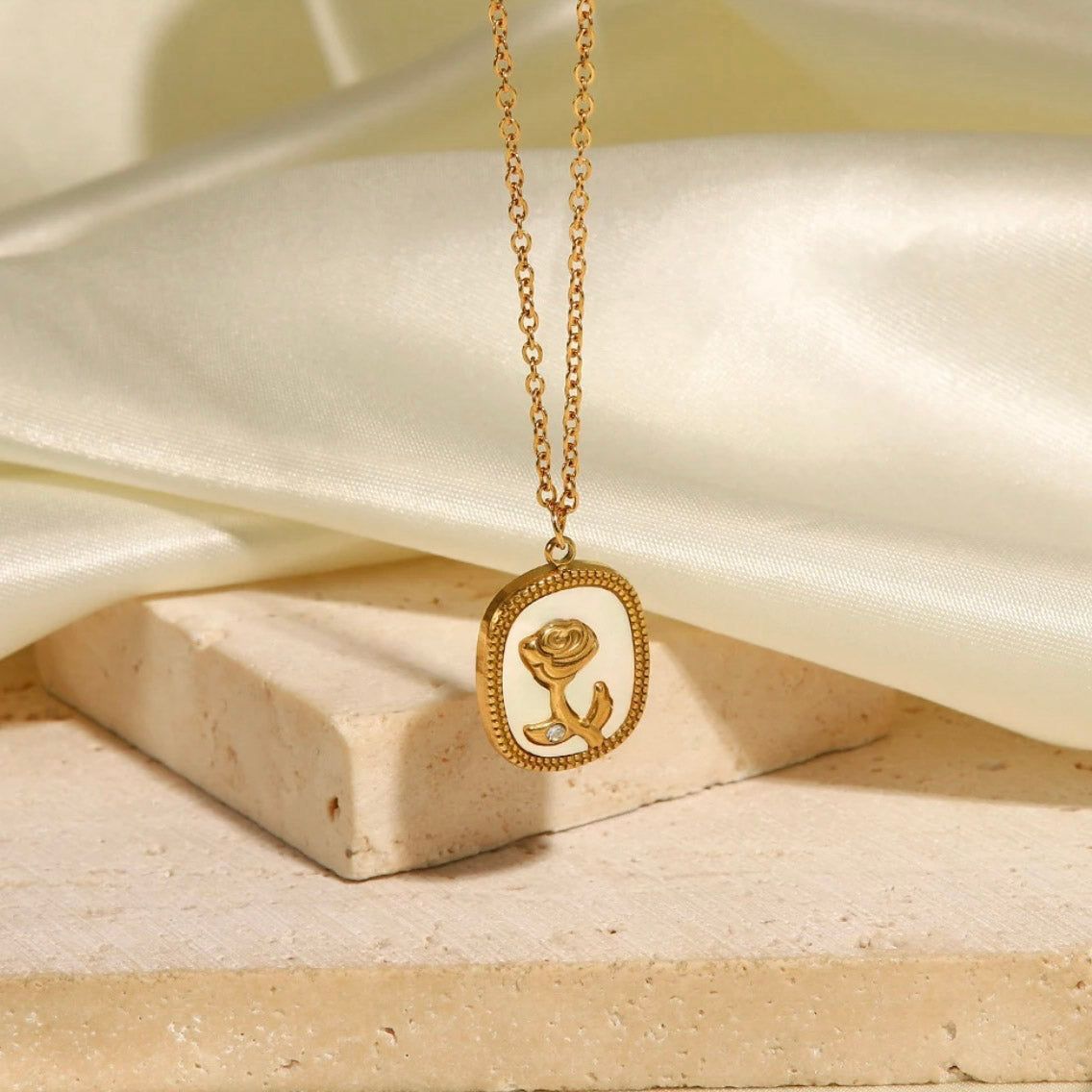 Gold necklace with a rose pendant on a beige surface