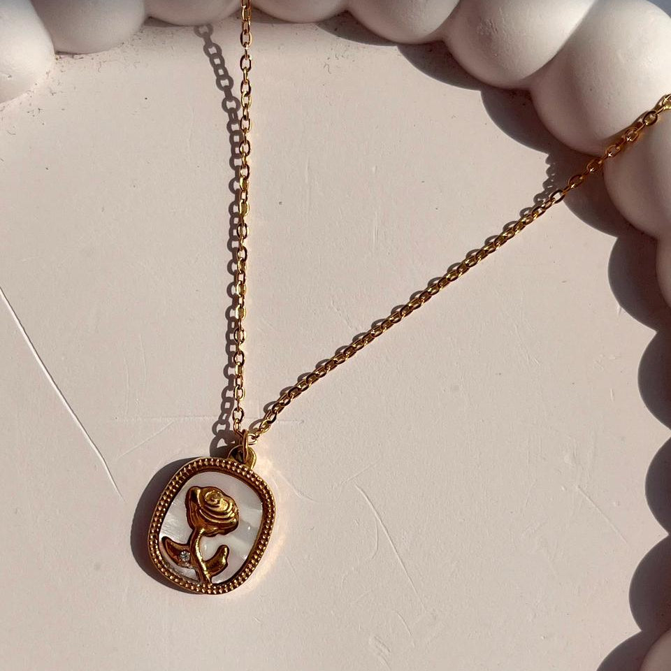 Gold necklace with a rose pendant on a light background