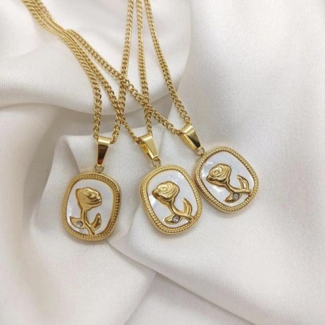 Three gold necklaces with rose pendants on a white fabric background