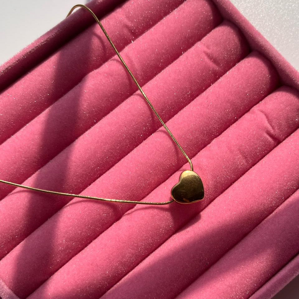 Gold necklace with a heart pendant on a pink velvet surface