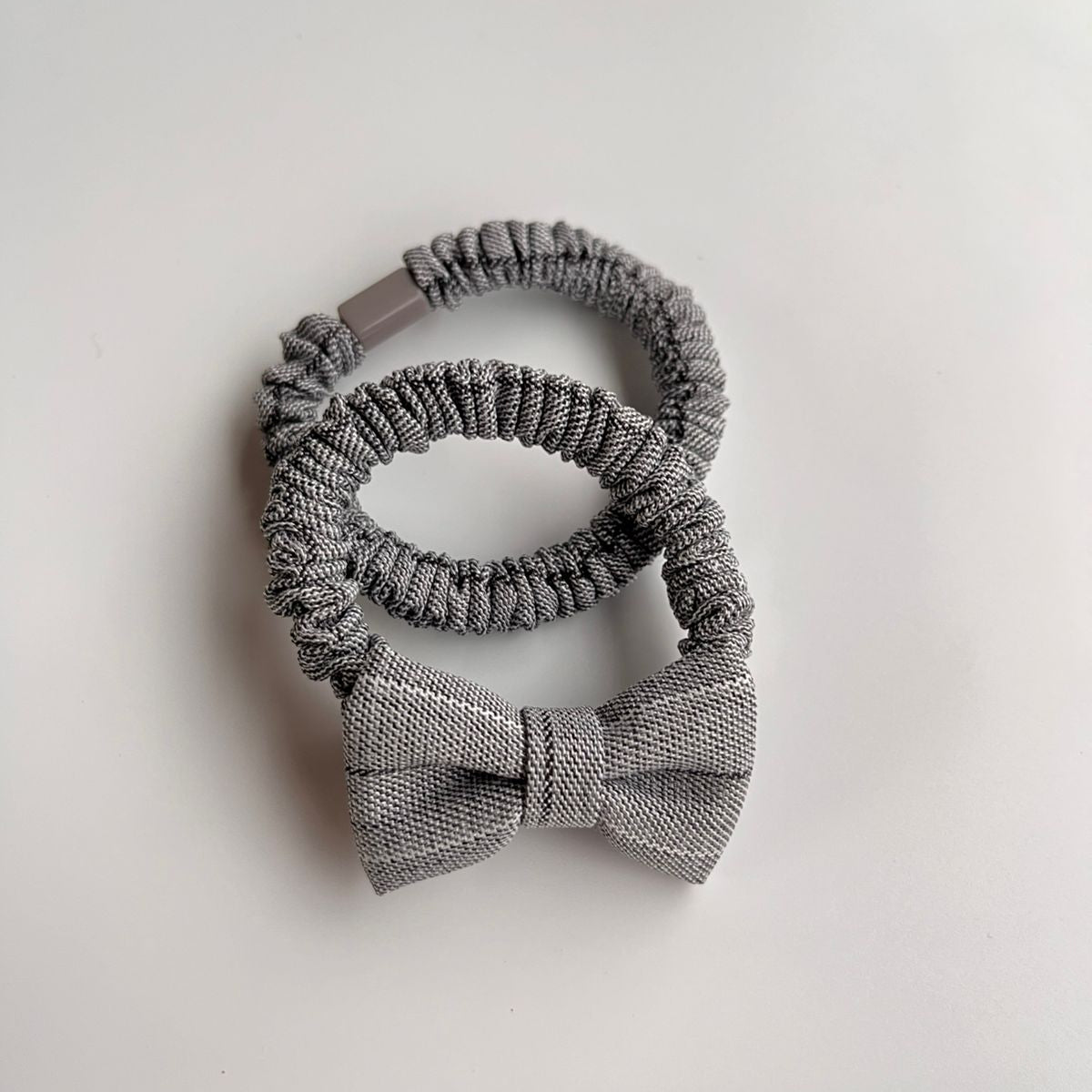Set of gray knitted hair accessories including a headband, scrunchies, and a bow on a light beige background.